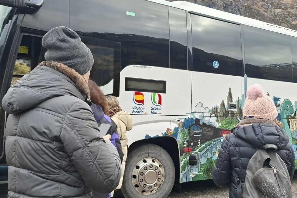 겨울 옷을 입은 사람들은 경치 좋은 삽화와 국기가 있는 장식된 투어 버스에 탑승하기 위해 줄을 서서 기다립니다.
