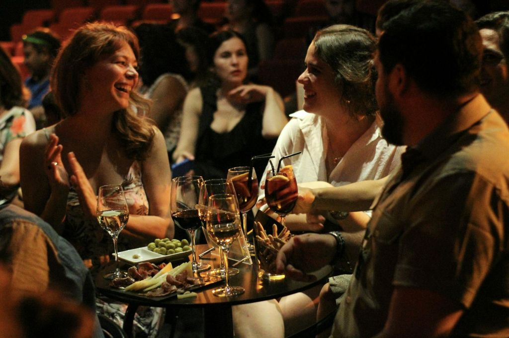 작은 테이블에 앉아 음료와 간식을 마시며 어둡게 빛나는 분위기에서 미소 짓고 대화하는 사람들.