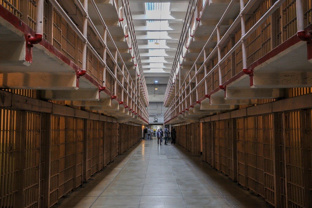 양쪽에 감방이 줄지어 있고 맨 끝에 몇 사람이 모여 있는 길고 텅 빈 감옥 복도.