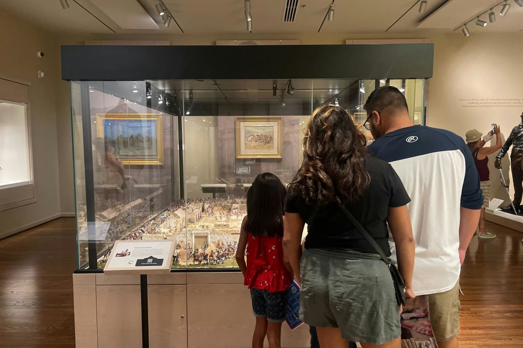 박물관에서 디테일한 디오라마를 관찰하는 사람들은 다른 방문객과 디스플레이를 배경으로 볼 수 있습니다.