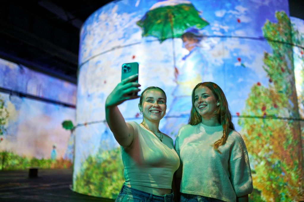 녹색 우산을 들고 있는 그림이 그려진 대형 스크린 앞에서 두 여성이 셀카를 찍기 위해 미소를 짓고 있습니다.