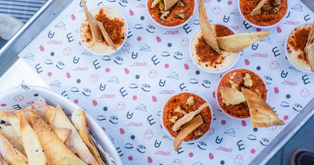 레드와 베이지 딥의 작은 그릇에는 브레드스틱과 너트가 장식되어 있으며, 디자인이 있는 무늬 종이에 놓여 있습니다.