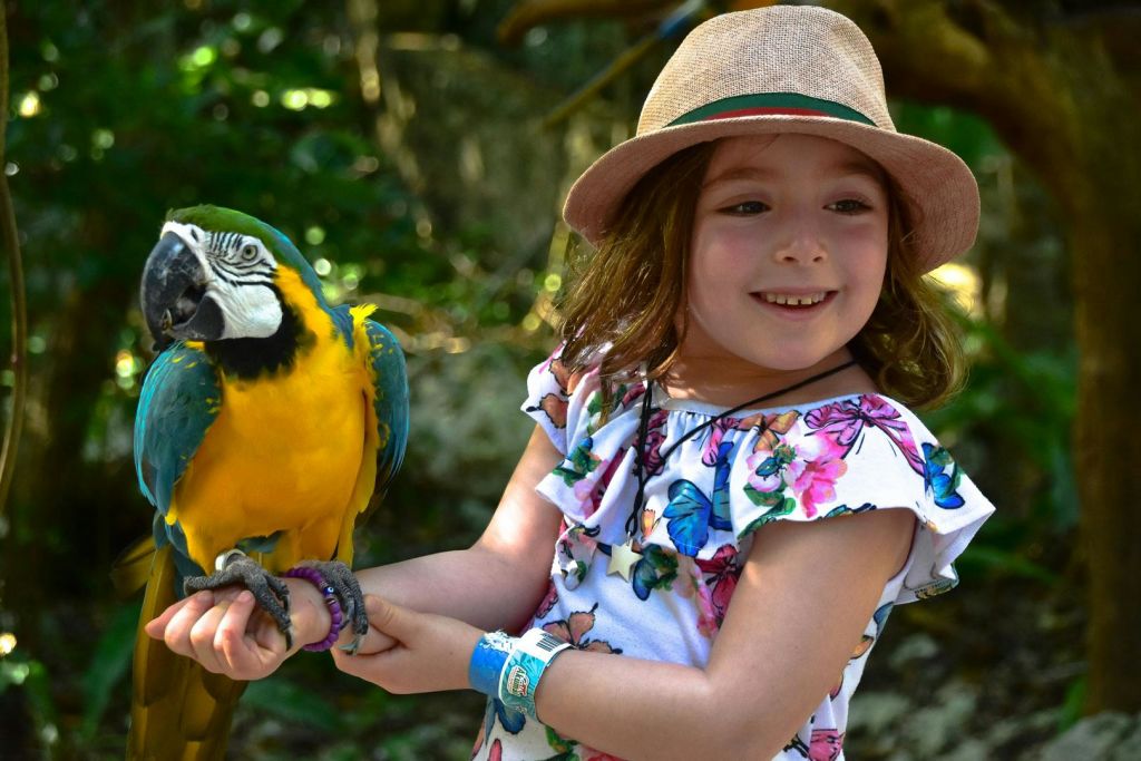 꽃무늬 드레스와 모자를 쓰고 야외에서 웃고 있는 어린 소녀. 왼쪽 손목에 파란색 손목 밴드가 있습니다.