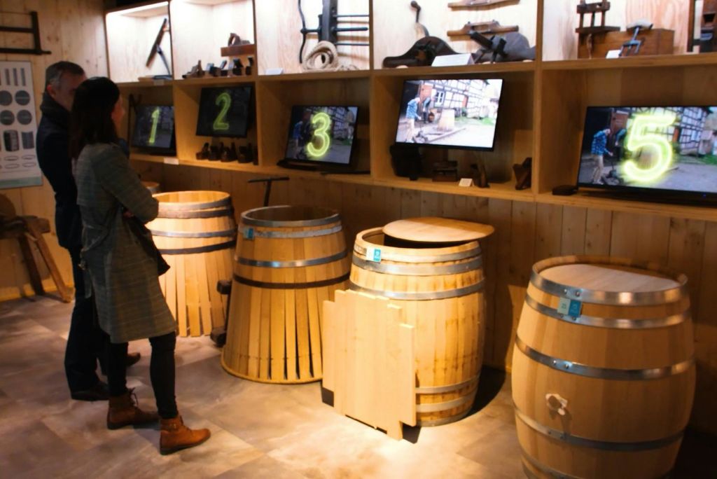 나무 전시 공간에는 나무 배럴과 인터랙티브 스크린 번호가 1 ~ 3번 적혀 있습니다. 사람이 화면을 관찰합니다.