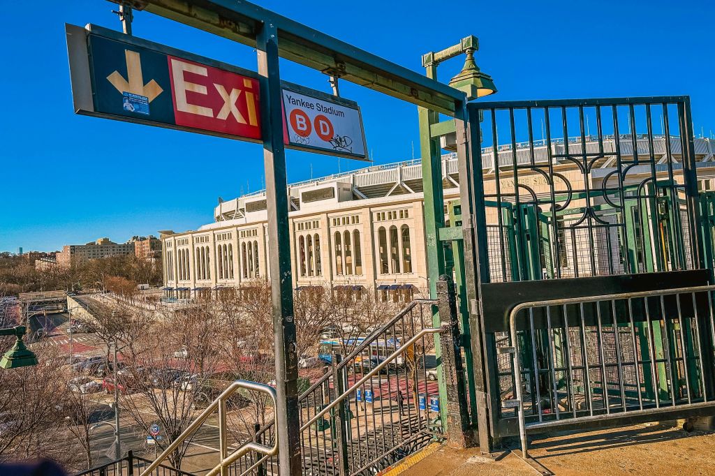 맑고 푸른 하늘 아래 양키 스타디움을 배경으로 플랫폼에서 내려오는 표지판과 계단을 빠져나오세요.