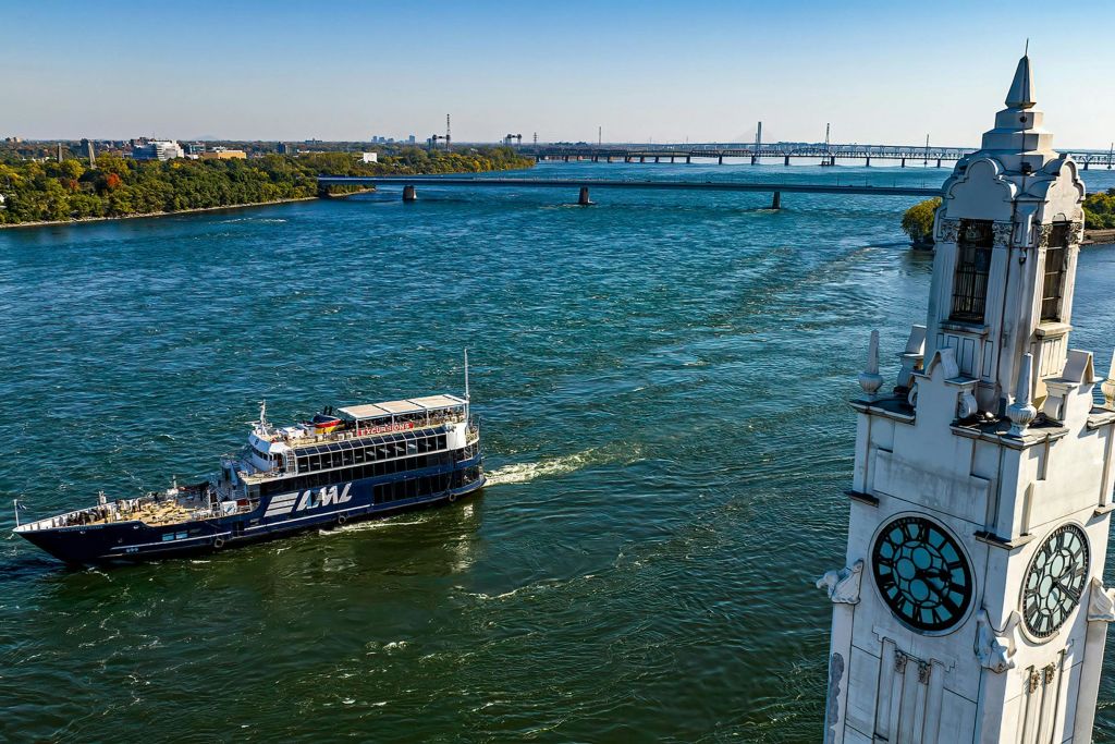 'AML' 이라고 표시된 여객선이 있는 강, 배경에는 다리가 있고, 앞쪽에는 시계가 있는 건물의 일부가 있습니다.