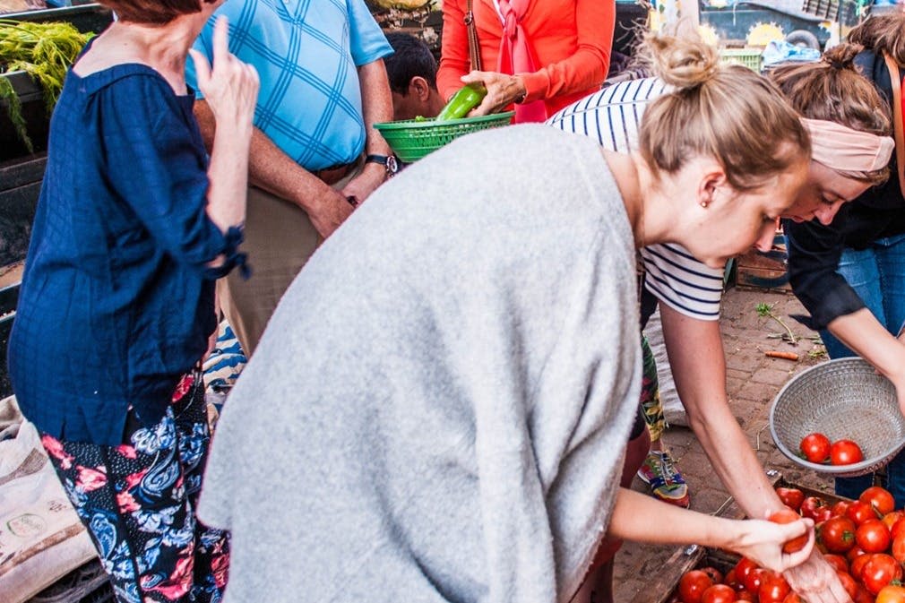야외 시장에서 쇼핑하고, 다양한 가판대에서 농산물을 찾아보고, 한 여성이 토마토를 따고 있습니다.