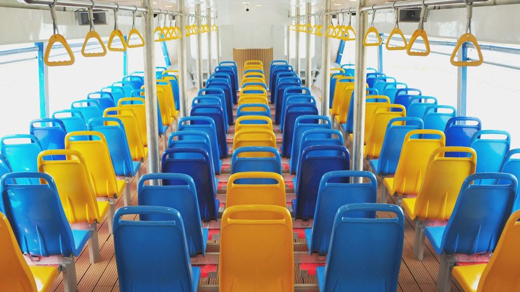 파란색과 노란색 플라스틱 좌석이 줄지어 있고 머리 위 노란색 난간이 있는 버스 내부.