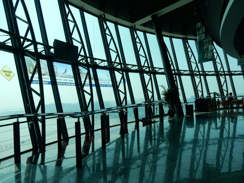 대형 창문, 금속 기둥, 반사 바닥이 있는 현대적인 유리벽 건물의 내부. 화분이 몇 개 보입니다.