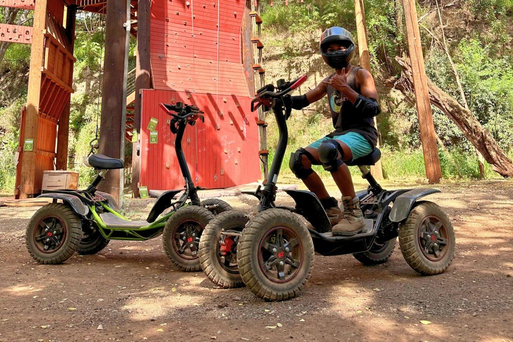 보호 장비를 착용한 사람이 다른 스쿠터 옆에 있는 오프로드 스쿠터에 앉아 있습니다. 등반 벽이 배경으로 보입니다.