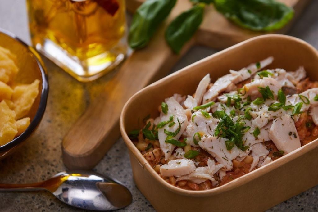 나무판에 숟가락과 아이스티 한 잔 옆에 잘게 썬 닭고기와 허브를 얹은 파스타 요리.