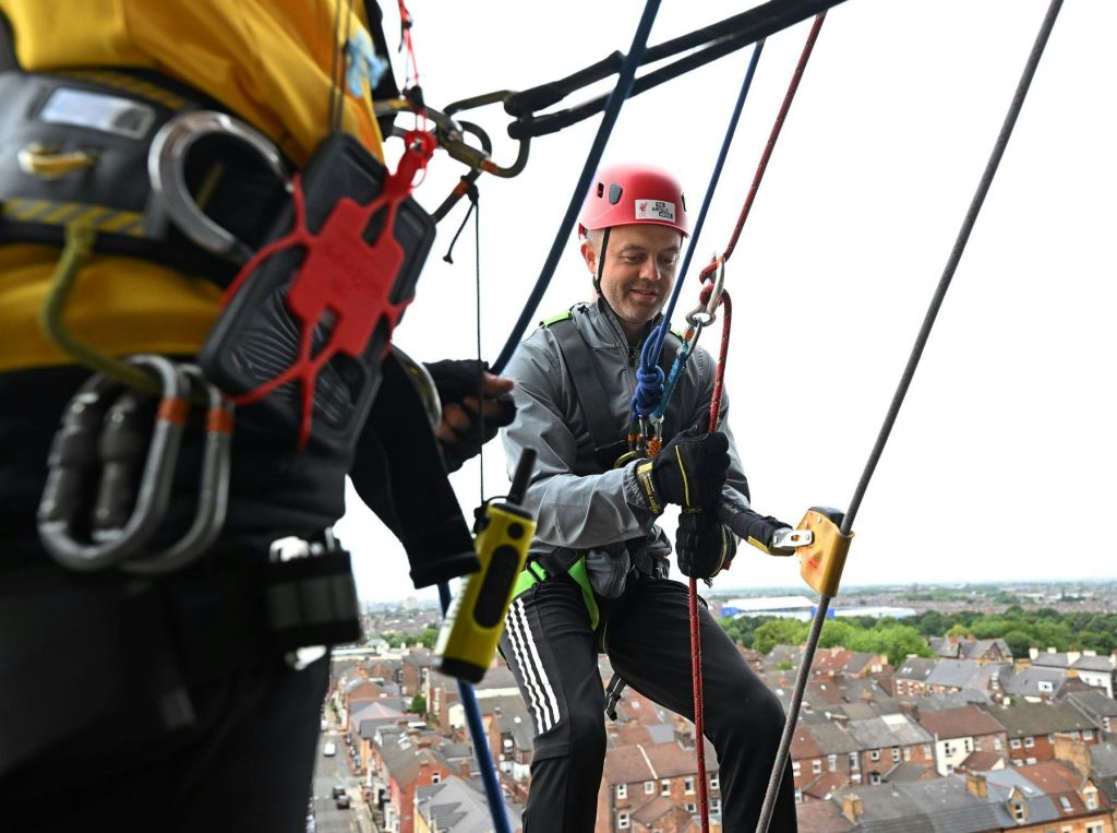 두 사람이 매달려 헬멧과 하네스를 착용한 채 건물 아래로 내려오고 있으며, 아래에는 주거 지역이 있습니다.