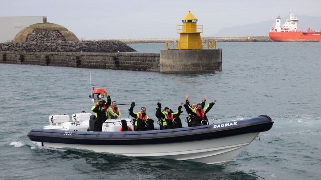 노란 등대가 있는 항구 근처에서 "다그마르" 라는 이름의 작은 보트를 타고 안전 장비를 착용한 5명이 물결을 이루고 있습니다.