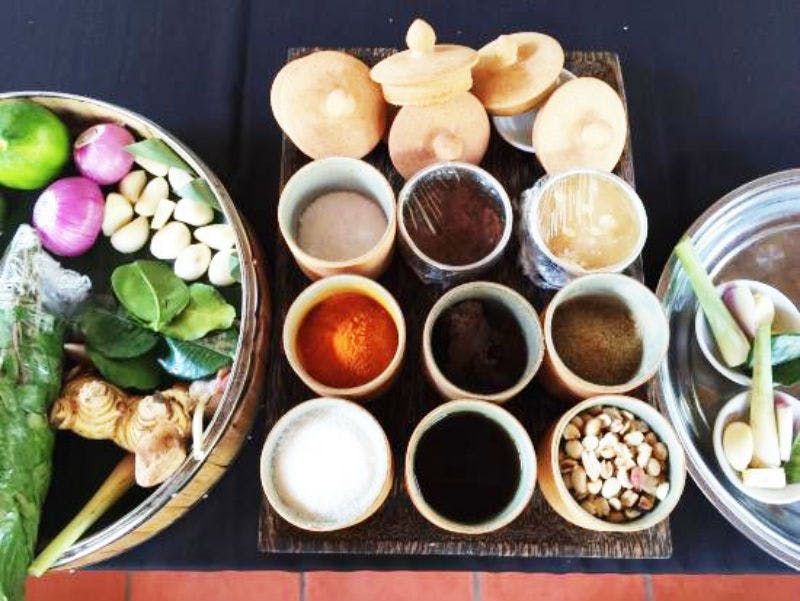 검은색 식탁보에 담긴 신선한 야채와 잎 바구니와 함께 작은 세라믹 용기에 담긴 다양한 향신료와 허브.