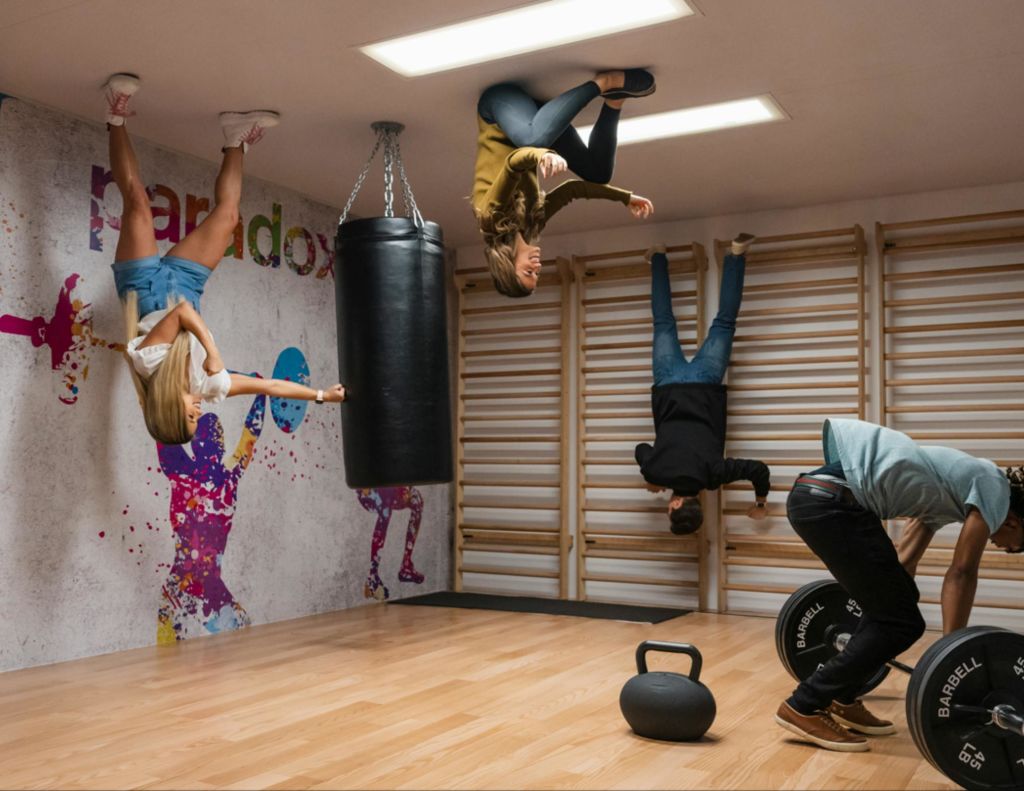 사람들은 천공 가방과 피트니스 장비를 바닥에 둔 채 체육관 천장에 서서 중력을 거스르는 것처럼 보입니다.