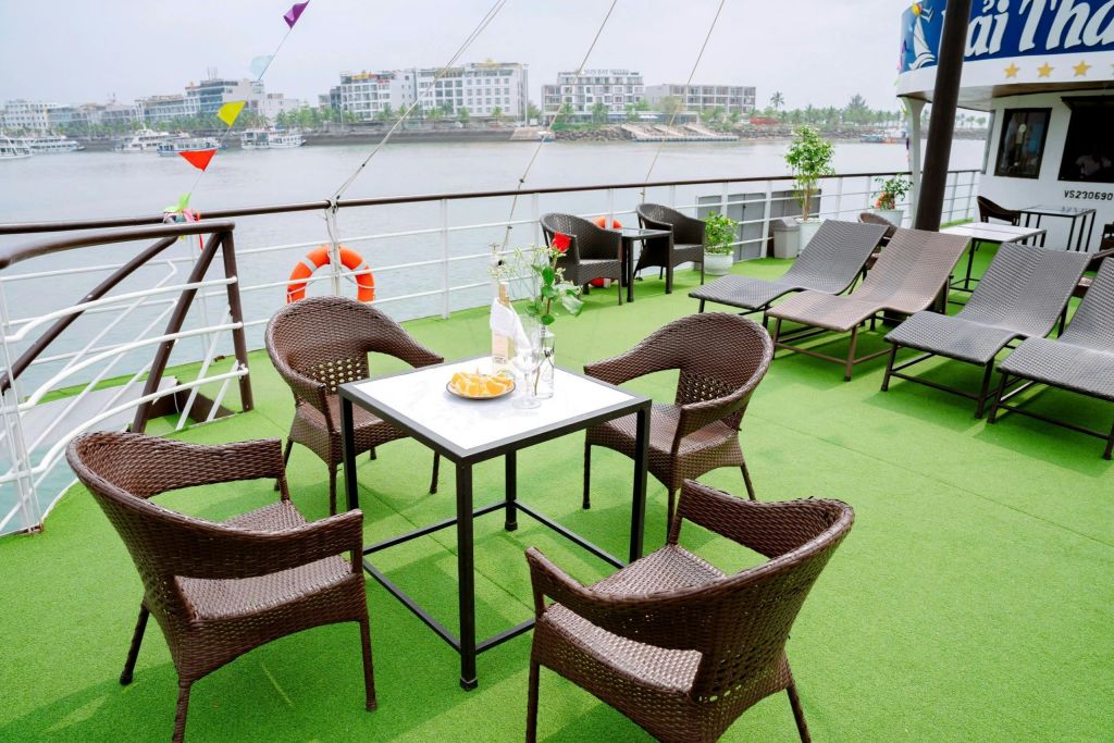 테이블 주변에 고리 버들 의자가 있는 보트의 야외 좌석 공간, 라운지 의자, 물과 건물을 배경으로 한 전망.