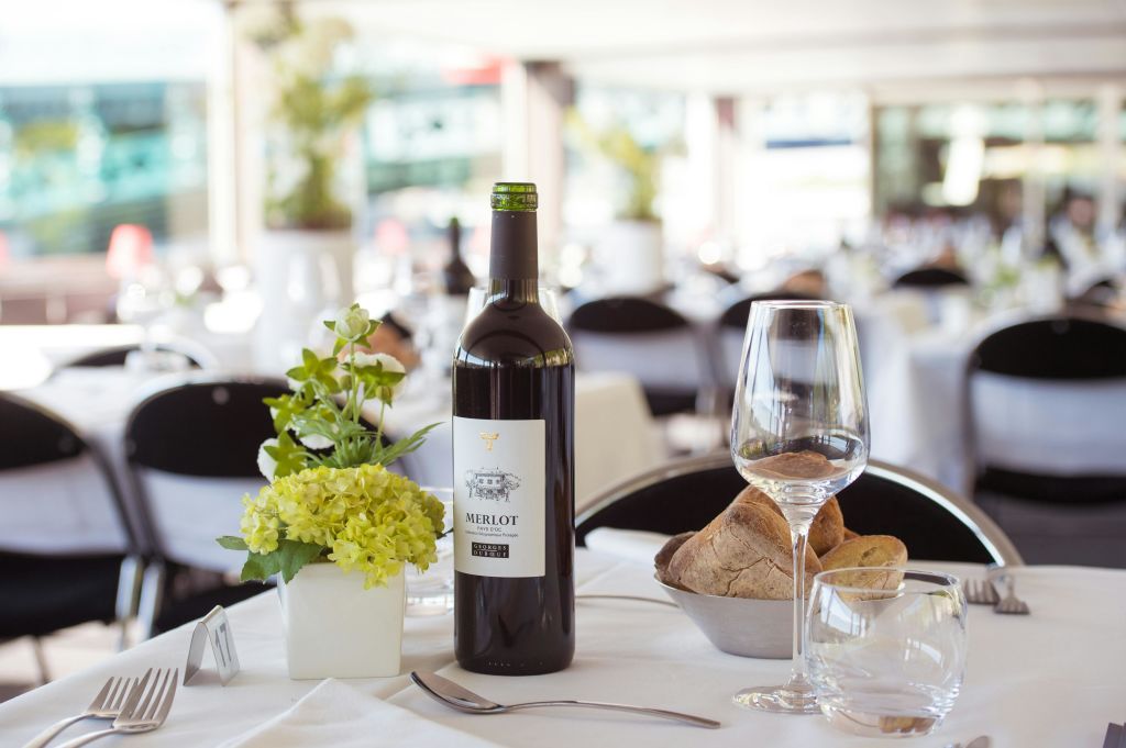 메를로 한 병, 그릇에 담긴 빵, 와인잔, 조명이 밝은 레스토랑의 물잔이 있는 우아한 테이블.