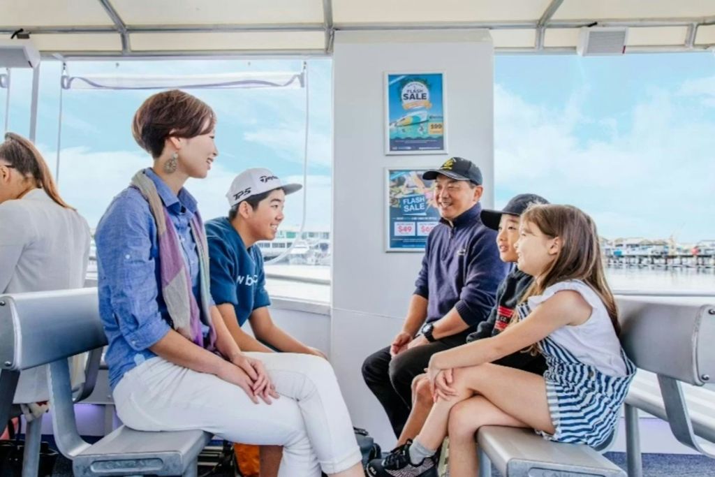 한 무리의 사람들이 보트에 앉아 대화를 나누고 있습니다. 창문 너머로 햇살이 내리쬐는 하늘과 물이 보입니다.