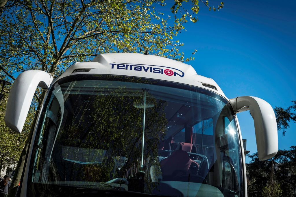 나무가 반사된 테라비전 버스의 전면 모습과 앞유리에 맑고 푸른 하늘이 있습니다.