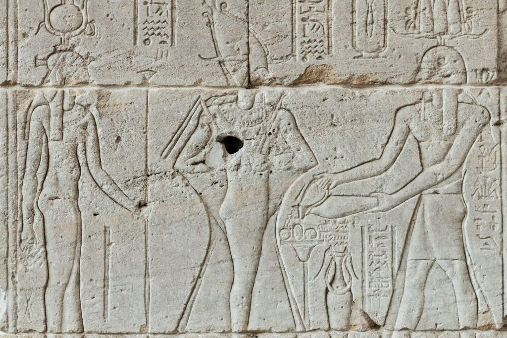 상형 문자로 둘러싸인 신의 프로필을 보여주는 고대 이집트 벽 조각과 의식용 물건을 들고 있는 것.