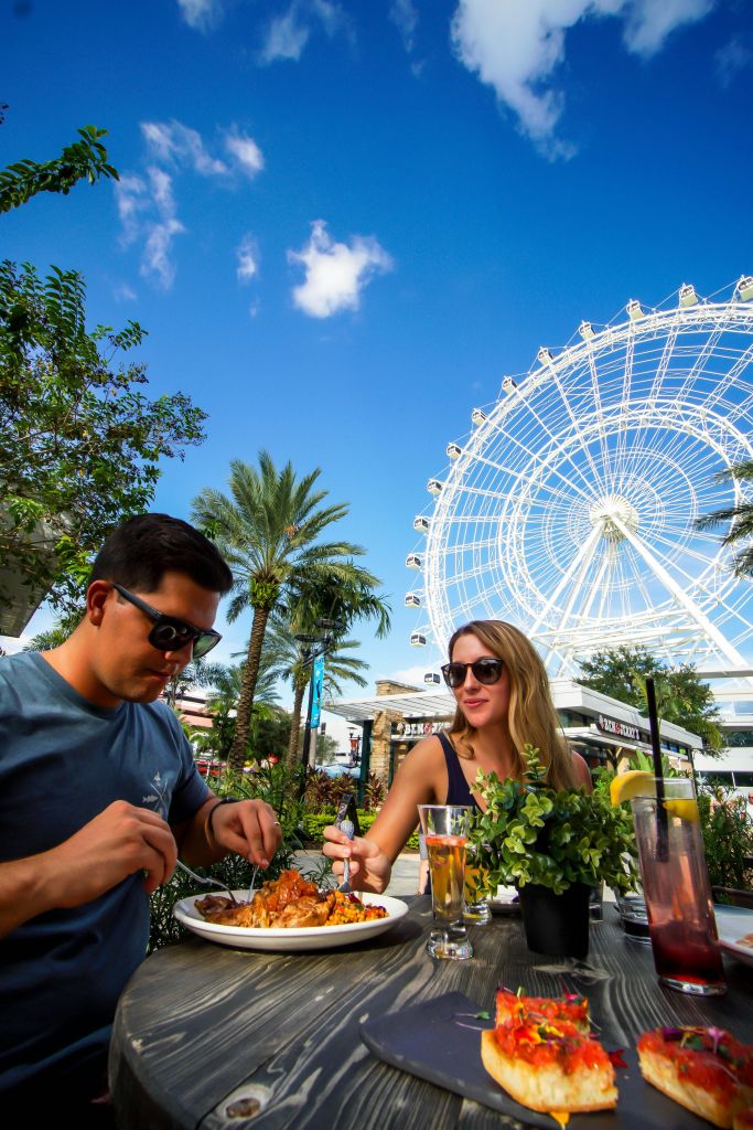 대관람차를 배경으로 야외에서 식사하는 남녀의 테이블에는 음식과 음료가 놓여 있습니다.