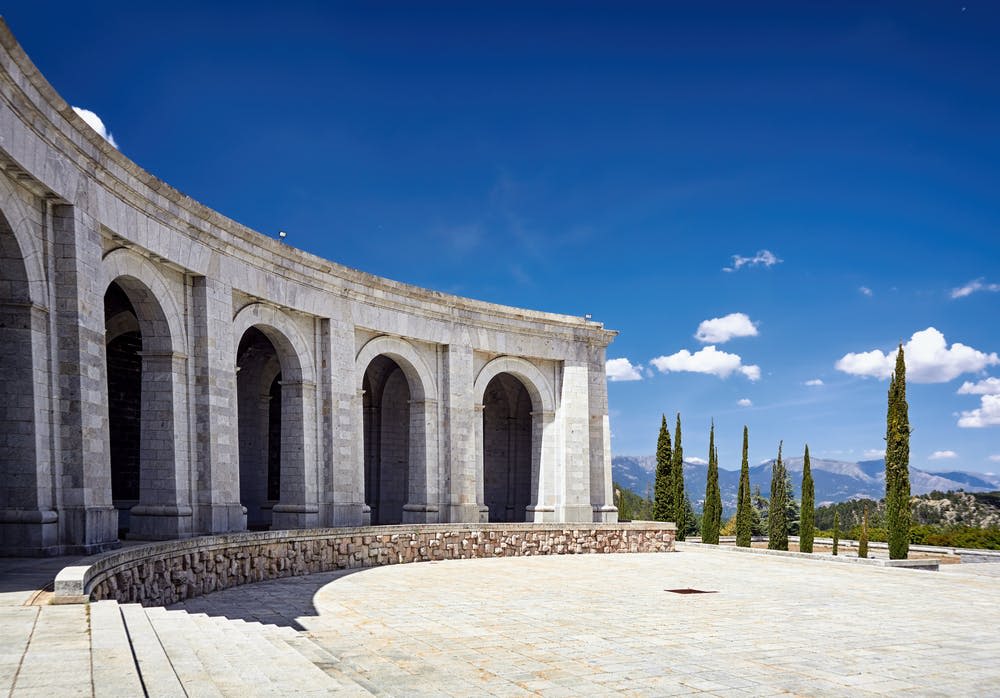 커다란 아치와 곡선형 외관이 있는 석조 건물이 맑고 푸른 하늘 아래 자리하고 있습니다. 키 큰 나무들이 배경을 이루고 있습니다.