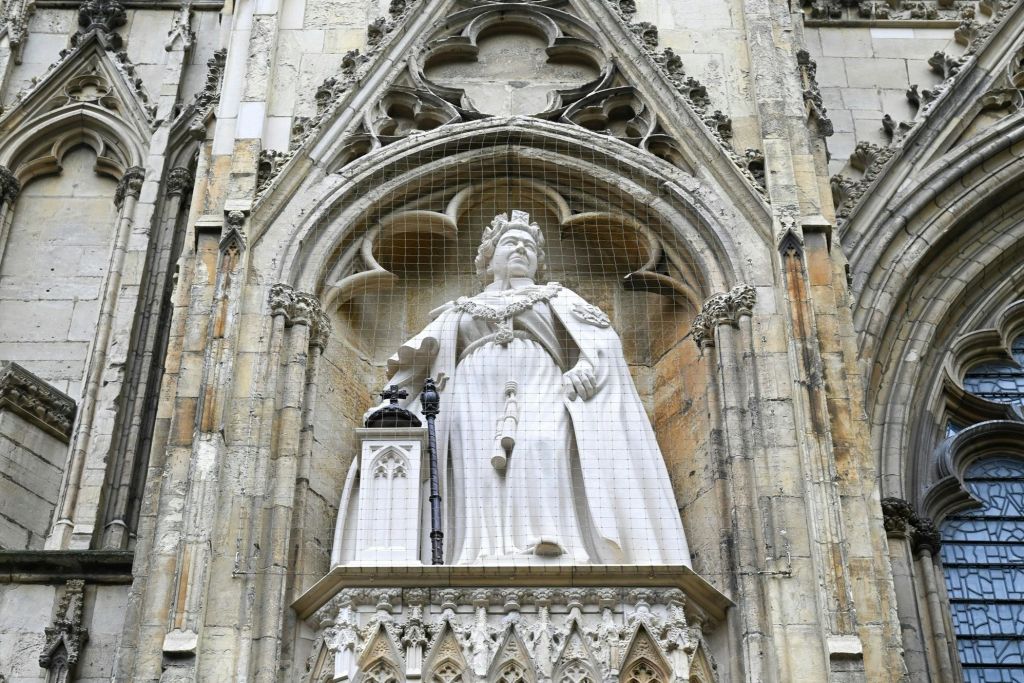 고딕 양식의 틈새시장에서 그물에 둘러싸인 왕실 복장을 한 역사적인 인물의 석상.