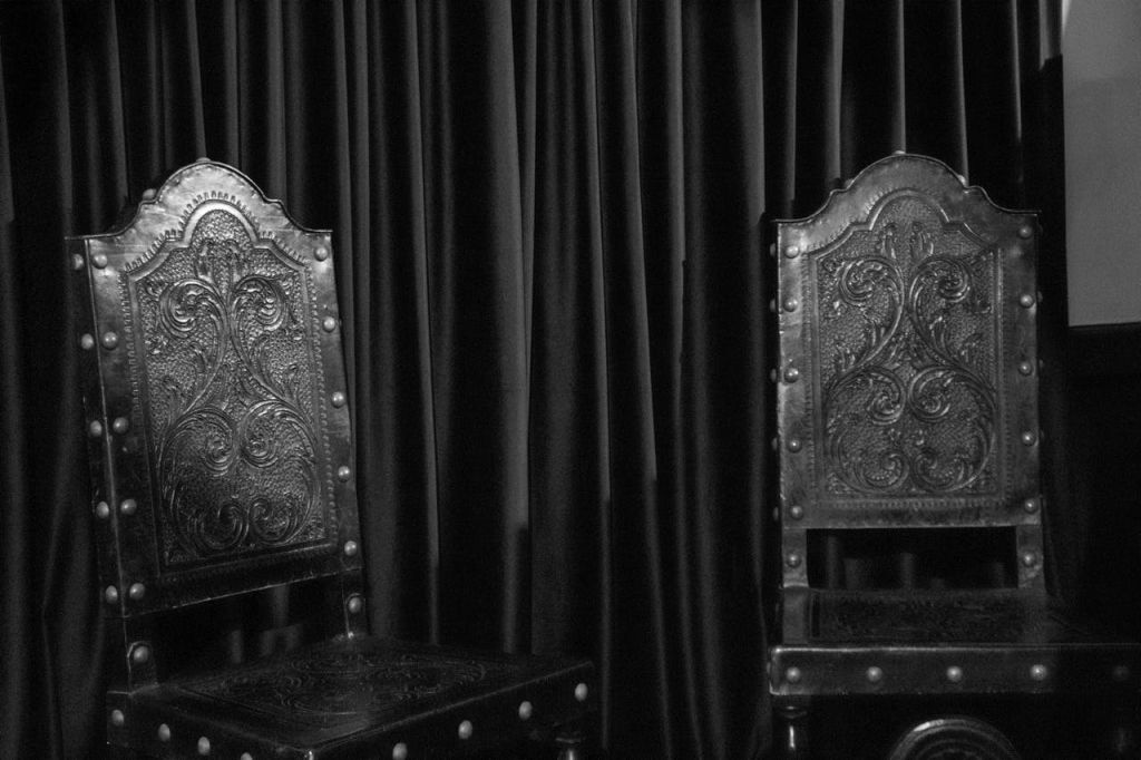 닫힌 어두운 커튼 앞에 정교한 조각이 있는 화려하고 어두운 나무 의자 2개.
