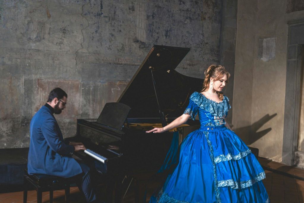 푸른색 드레스를 입은 한 여성이 질감이 살아있는 벽이 있는 어두운 방의 그랜드 피아노 근처에 서 있습니다.