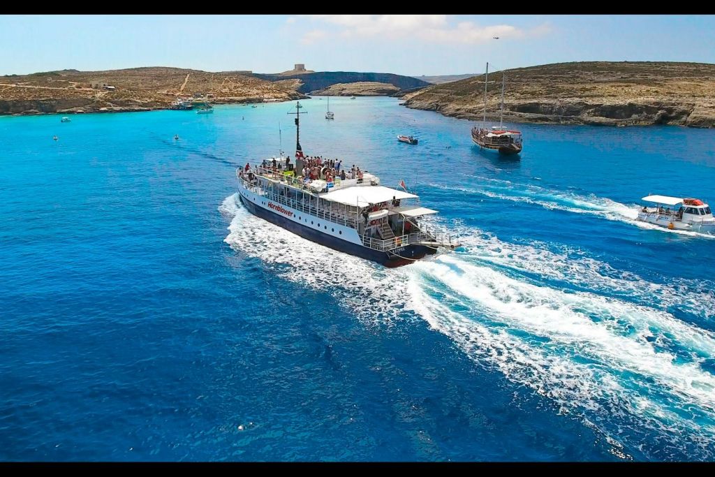 승객이 탑승한 대형 보트가 바위 해안가 근처의 맑고 푸른 바다를 항해합니다. 배경에는 작은 보트 두 척이 있습니다.