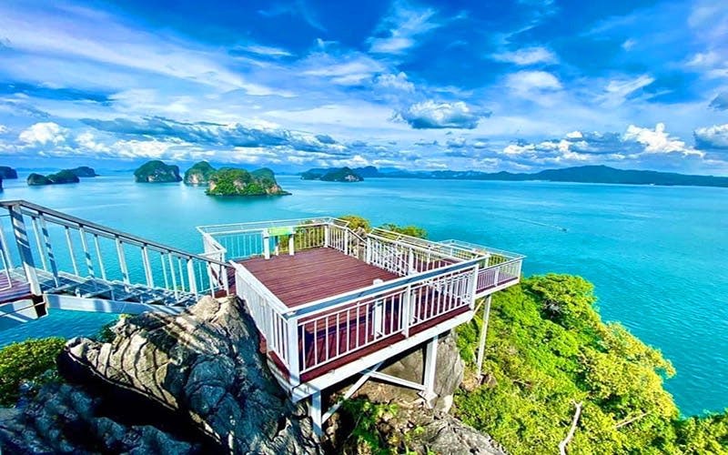 드넓은 바다와 푸른 섬, 구름이 흩날리는 맑고 푸른 하늘이 내려다보이는 하얀 난간이 있는 목조 전망대.