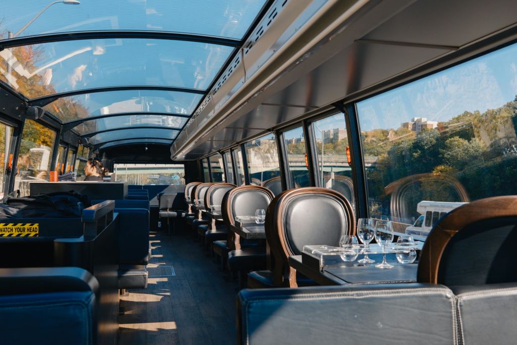 유리 지붕, 파란색 좌석, 유리 제품으로 세팅된 테이블이 있는 텅 빈 기차 식당 차량의 내부로, 경치 좋은 녹지가 내려다보입니다.