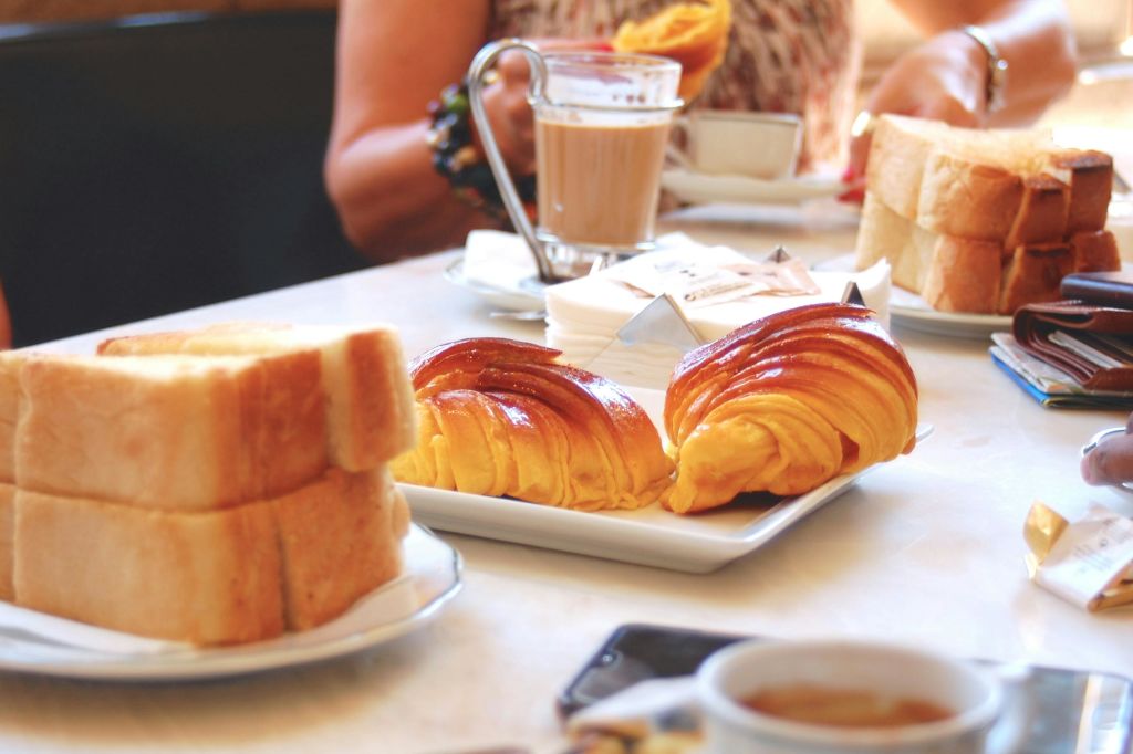 크루아상, 얇게 썬 빵, 커피, 패스트리와 음료를 들고 있는 사람들과 함께 아침 식사를 할 수 있는 테이블입니다.