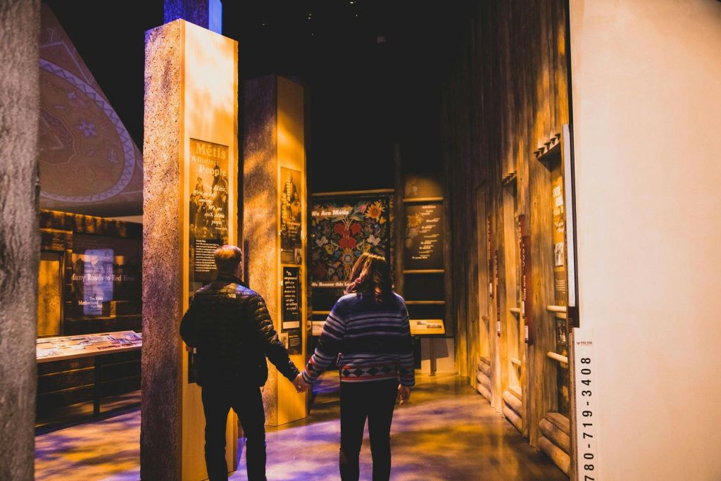 벽에 안내 패널이 놓인 희미한 조명의 박물관 전시관을 두 손을 잡고 걸어보세요.