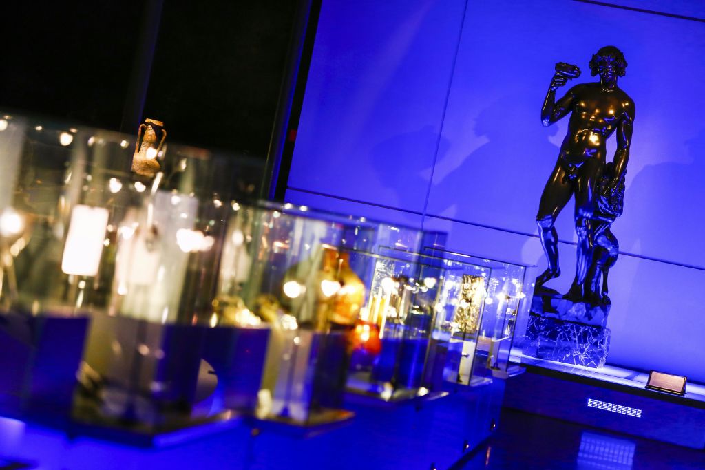 다양한 조명 유물이 있는 유리 디스플레이 케이스. 파란색 조명 벽을 배경으로 물건을 들고 있는 사람의 동상이 있습니다.