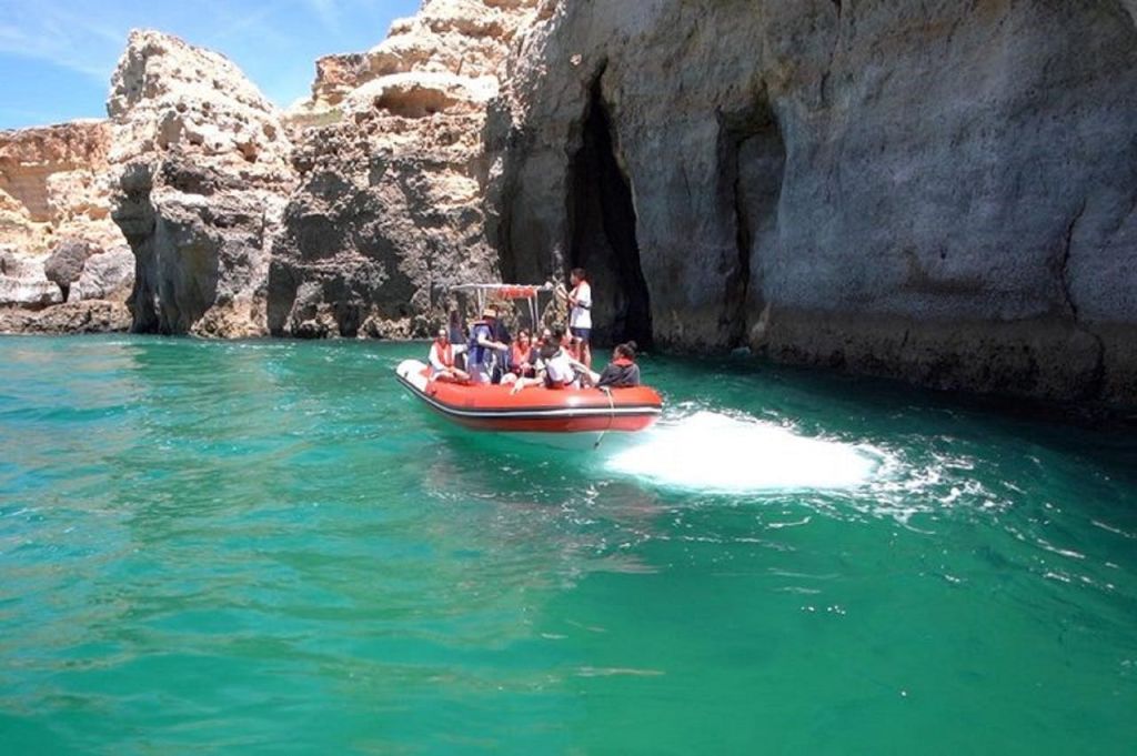 청록색의 맑은 물 위 바위 동굴 근처에서 팽창식 보트를 타고 있는 한 무리의 사람들.