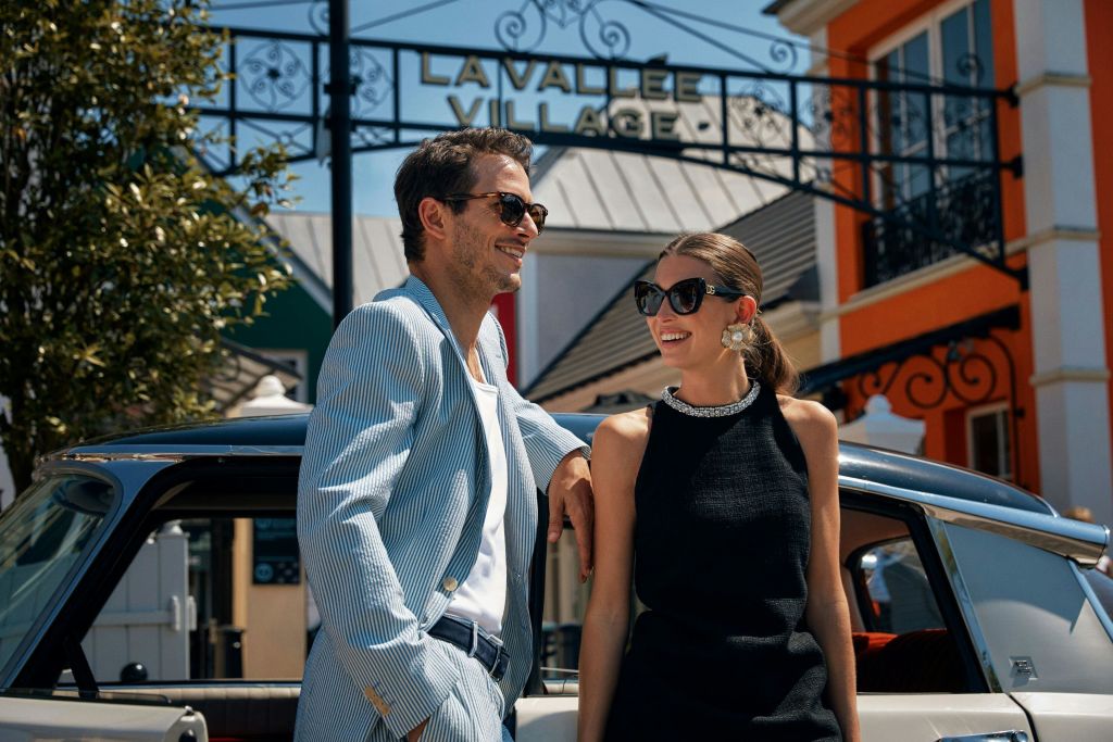 화창한 날 라 발레 빌리지 쇼핑센터 밖에서 세련된 의상을 입은 한 남녀가 웃고 있습니다.