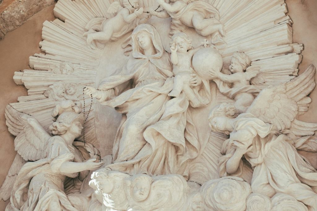 천사에 둘러싸인 아이를 안고 있는 중앙 가운을 입은 여성을 포함한 종교적 인물을 묘사한 정교한 석조 부조.