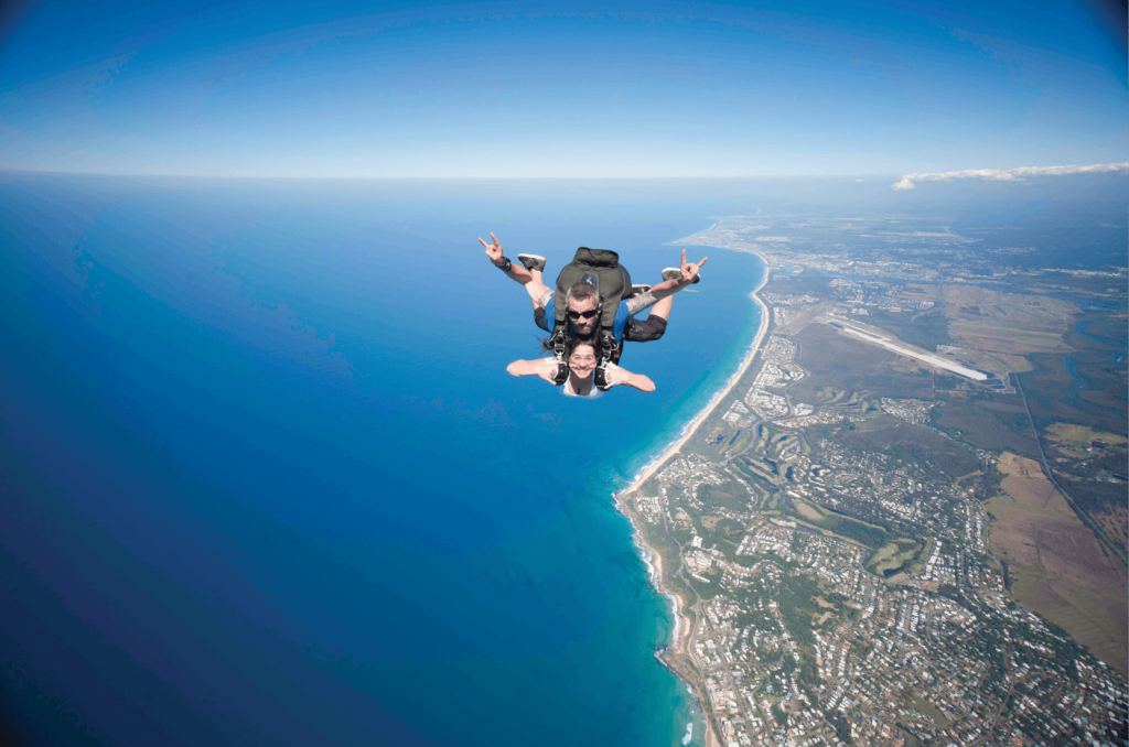 바다가 왼쪽에 있고 건물과 도로가 오른쪽에 있는 해안 풍경을 감상하며 스카이다이빙을 즐기는 두 사람.