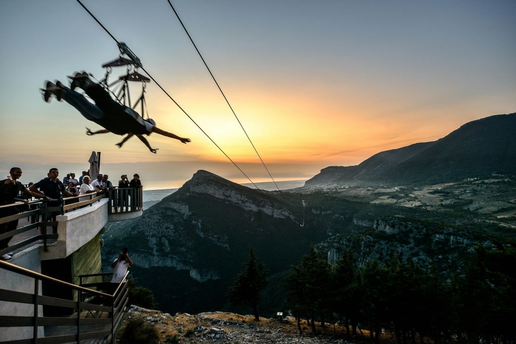 플랫폼에서 관찰자와 함께 일몰에 산악 풍경 위에 지퍼 라이닝을 하는 사람.