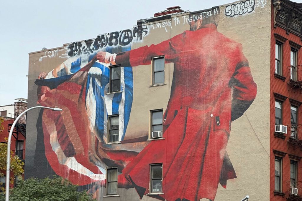 빨간색 옷을 입은 사람이 파란색과 흰색 옷을 입은 사람과 손을 잡는 모습을 그린 건물의 대형 벽화. 상단에 그라피티가 보입니다.