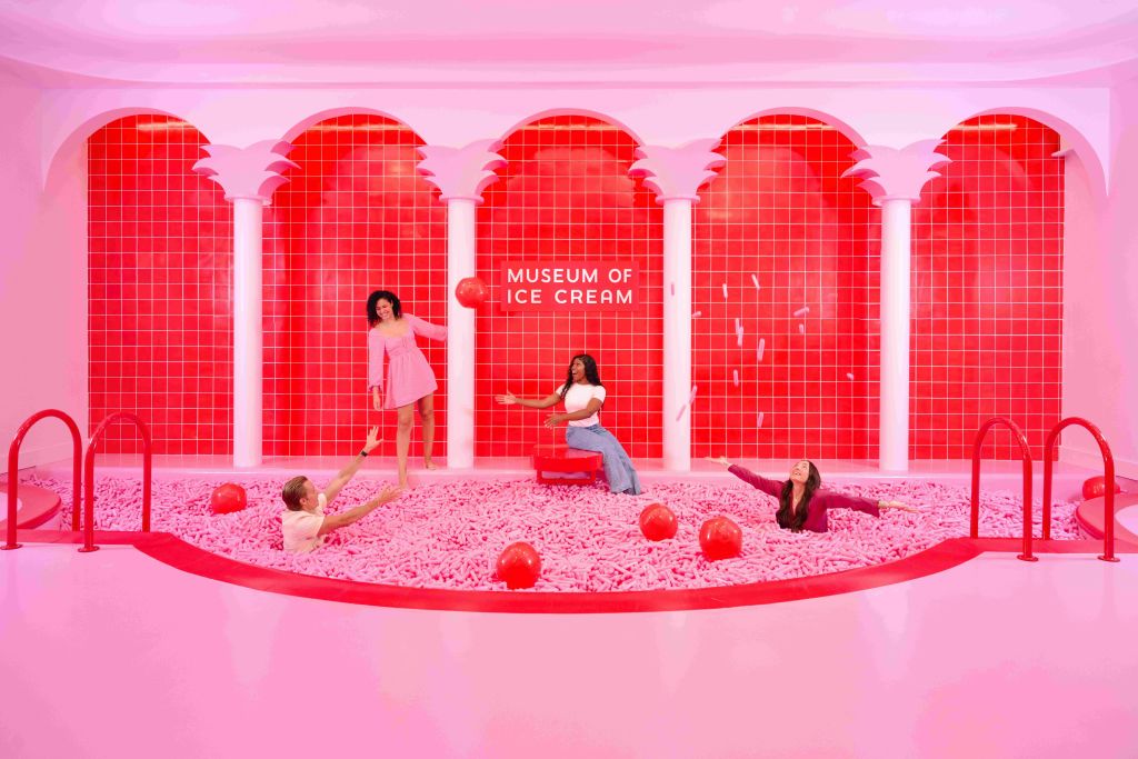 빨간색 공이 있는 분홍색 공 구덩이에서 '아이스크림 박물관' 이 적힌 빨간색 타일 벽 앞에서 4명이 놀고 있습니다.