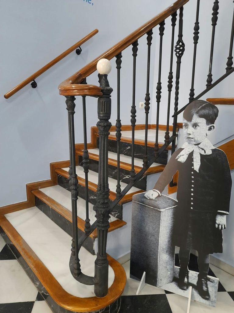 나무 난간과 검은 금속 난간이 있는 계단입니다. 계단 옆에는 어린 소년의 흑백 컷아웃이 서 있습니다.