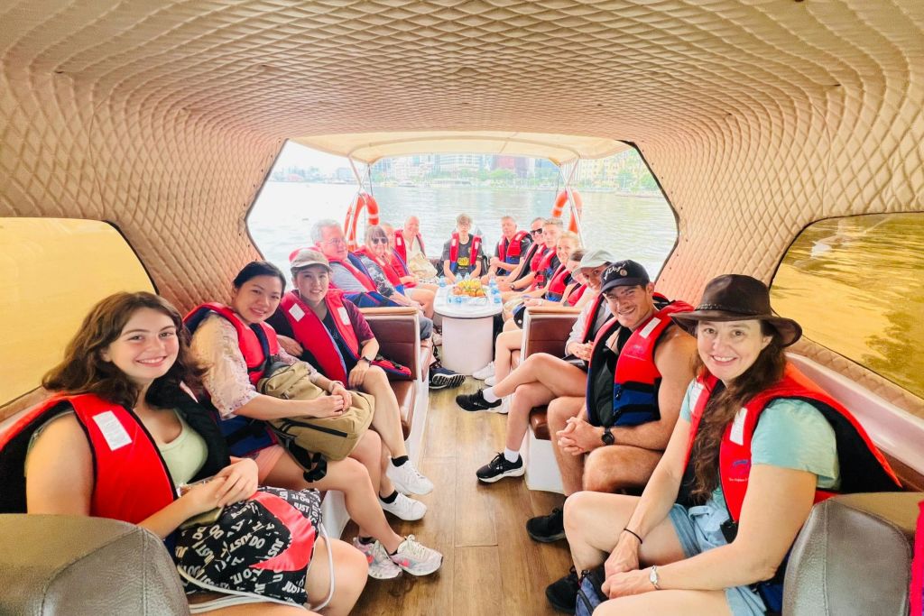 빨간 구명조끼를 입은 미소 짓는 사람들이 창문 너머로 보이는 도시 풍경을 조망할 수 있는 보트 안에 앉아 있습니다.