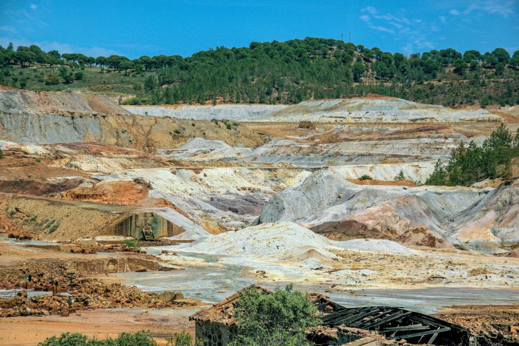 노출된 대지와 광물 매장지 층이 있는 광활한 광산 지역, 맑은 하늘 아래 푸른 숲이 우거진 언덕.