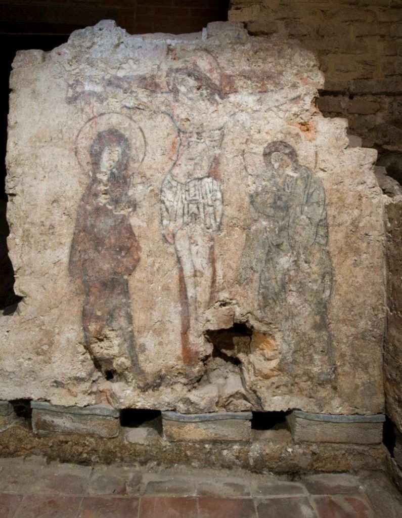 거친 돌담에 그려진 중앙 십자가 형상을 포함한 퇴색된 세 인물의 고대 벽화는 부분적으로 악화되었습니다.