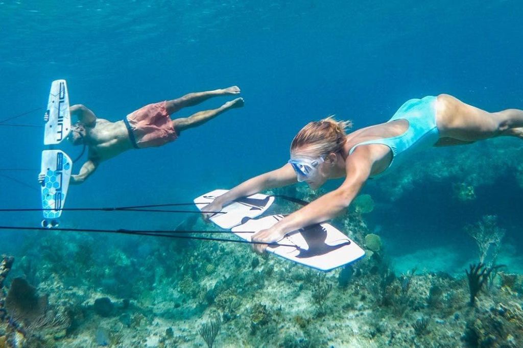 두 사람이 산호초 너머로 물속에서 스노클링을 하고 있습니다. 한 사람은 하얀 바다 스쿠터를 잡고 있습니다.
