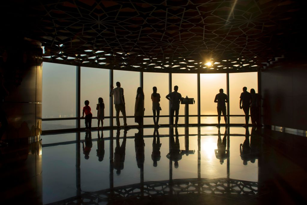커다란 창문, 기하학적 천장 패턴, 햇살이 비치는 방에 사람들의 실루엣이 서 있습니다.