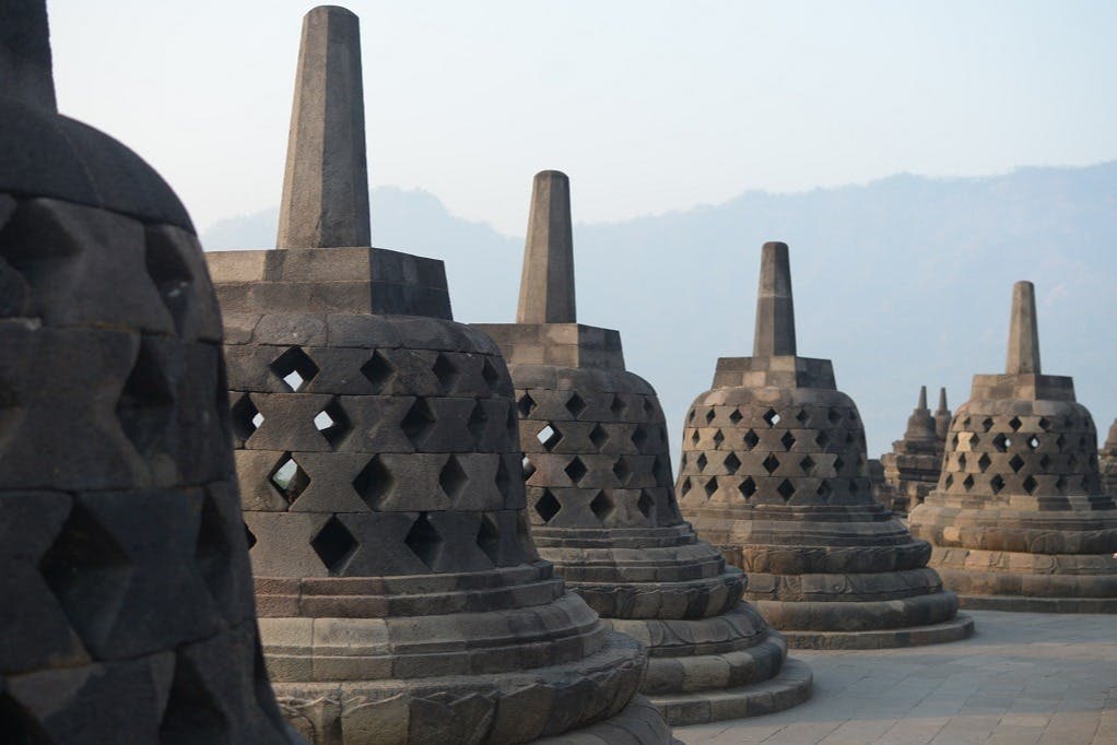 산을 배경으로 산이 희미하게 보이는 보로부두르 사원의 정교한 문양이 돋보이는 석조 조각상.