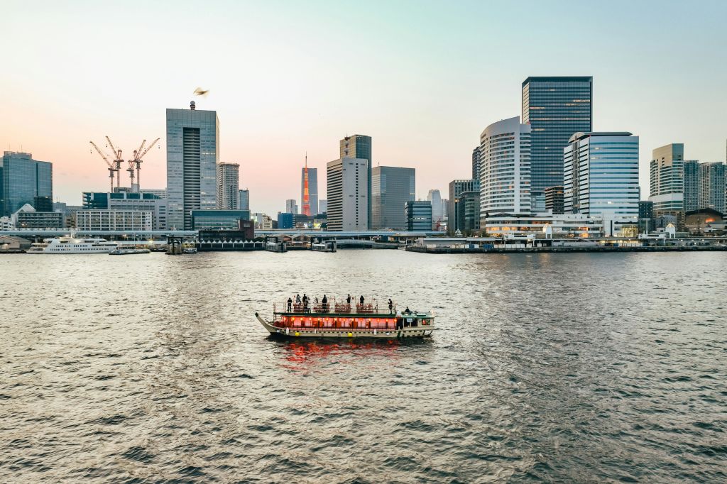 석양이 질 때 도시의 고층 빌딩을 배경으로 강에서 승객과 함께 조명이 켜진 투어 보트.